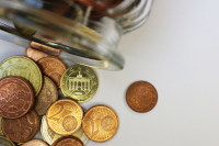 Euromünzen liegen vor einem umgefallenen Glasgefäß