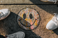 zwei Personen in weißen Sneaker stehen um einen auf den Boden gemalten, lächelnden Smiley